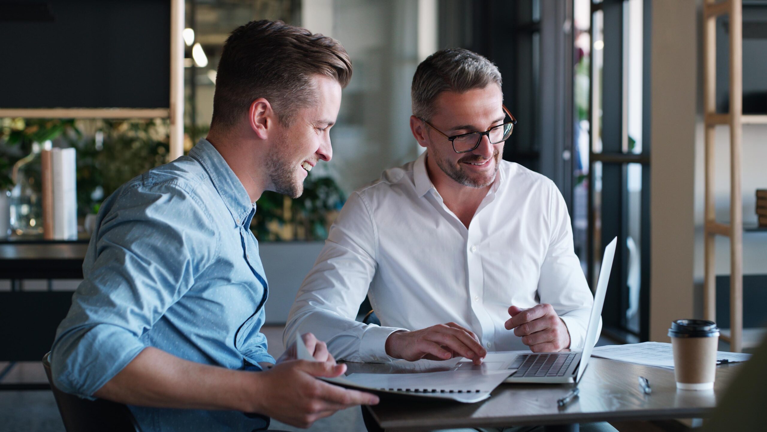 Shot of two businessmen using a laptop and having a discussion in a modern office